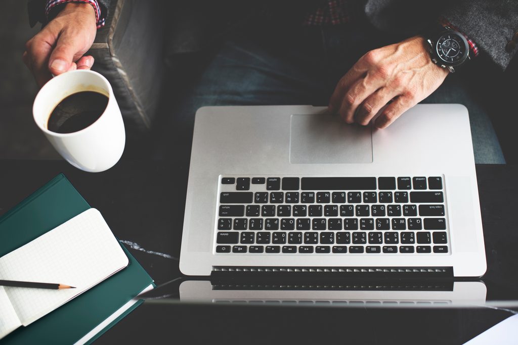Business professional working at a laptop with notebook and coffee